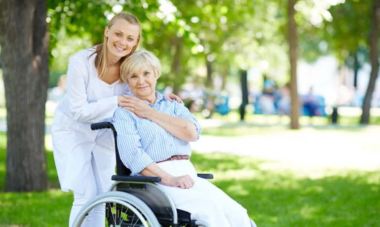 Pflegerin mit Seniorin im Rollstuhl im Park